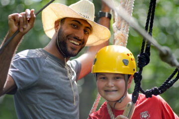 A staff member poses with a camper while on a High Ropes activity