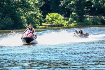 Staff member driving a jet ski pulling two campers on a tube